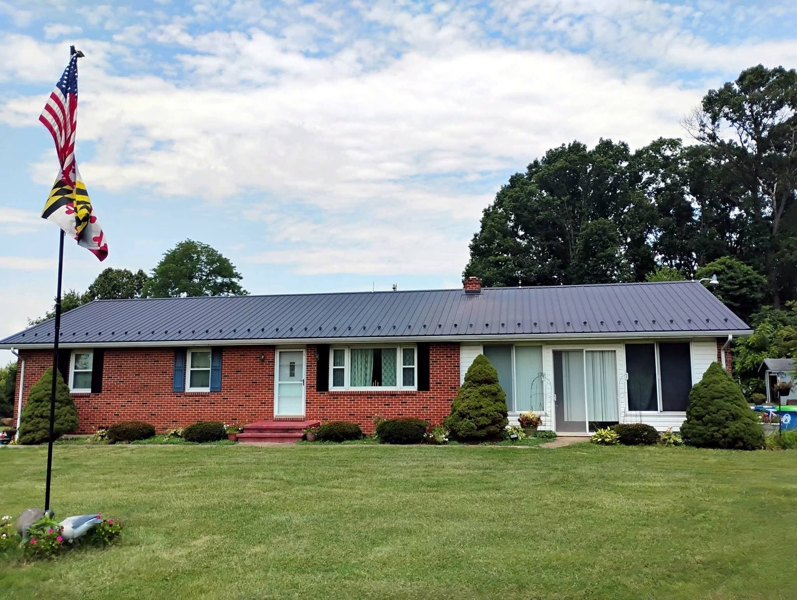 Finished brick ranch home with a dark metal roof